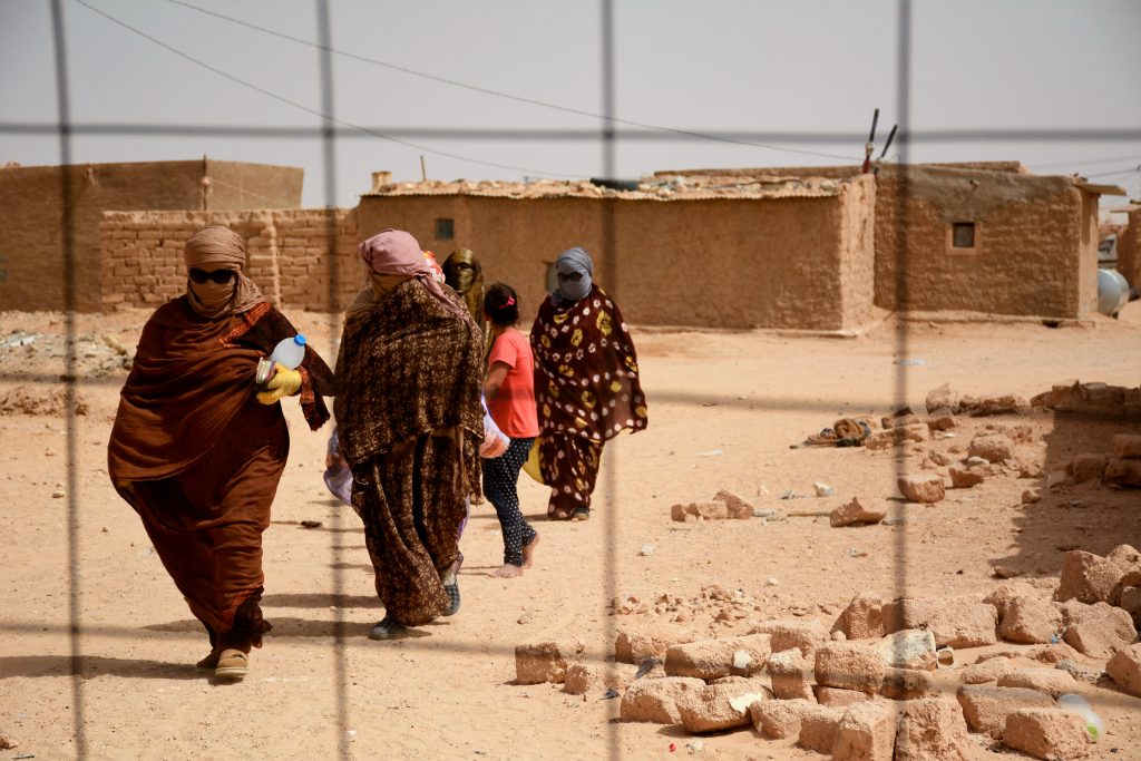 Kvinnor iklädda melfor går i en klunga i de västsahariska flyktinglägren. Ett nät syns framför dem.